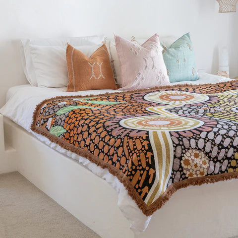 Bed with a colorful patterned throw blanket and decorative pillows in a bedroom setting.