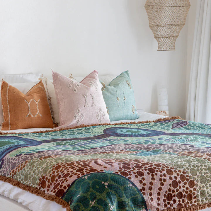 Colorful patterned blanket on a bed with decorative pillows against a white wall.