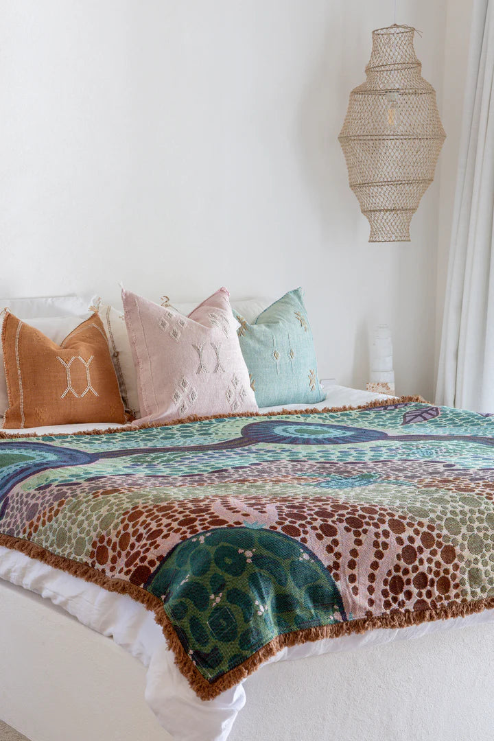 Colorful patterned blanket on a bed with decorative pillows against a white wall.