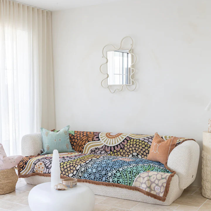 Decorative quilt on a white sofa in a bright living room with a mirror and cushions.