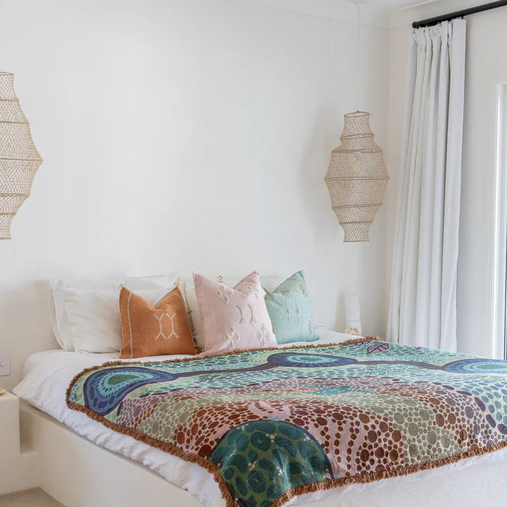 Bedroom with a bed featuring a colorful blanket and pillows, wooden ceiling fan, and decorative lamps.