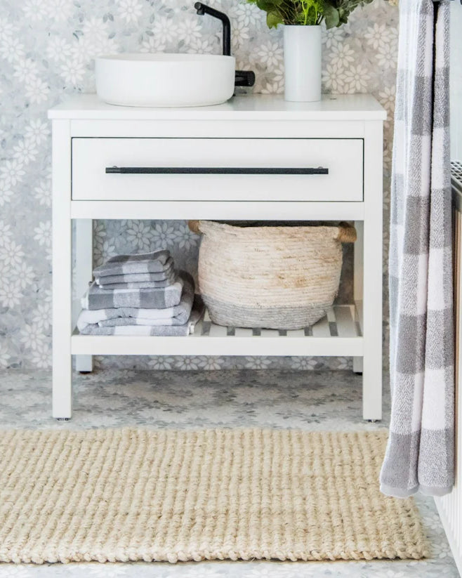 Bathroom with white vanity, towels, and a rug on a light gray floor.