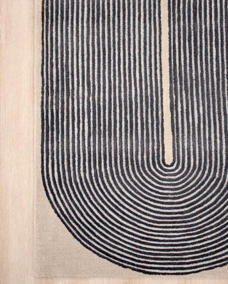 Close-up of a modern area rug with a U-shaped design featuring concentric arches in black on a beige background, shown on a light wood floor.