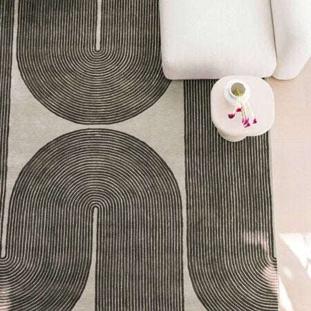 Gray area rug with black abstract patterns on a light-colored floor.