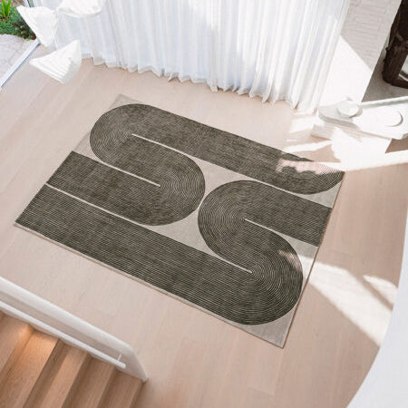 A rectangular area rug with a modern abstract design of two large winding dark gray loops on a light beige background, styled on a light wood staircase landing.