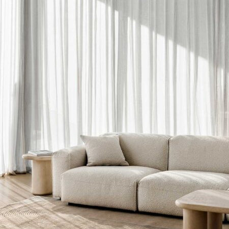 Beige sofa in a modern living room with light curtains and wooden coffee tables.
