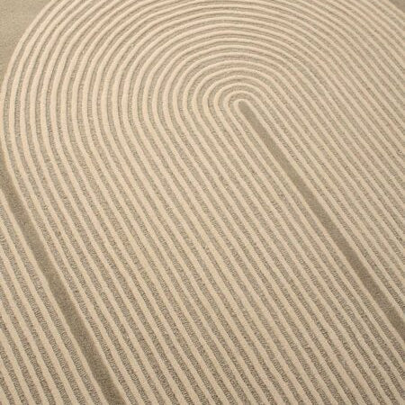 A close-up of a textured area rug featuring a modern, minimalist concentric arch pattern in warm beige and cream tones.