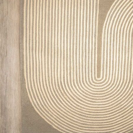A close-up of a rug with a geometric pattern of concentric arches in cream on a taupe background, shown on a light wood floor.