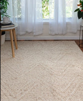 Beige woven rug in a room with white curtains and plants.