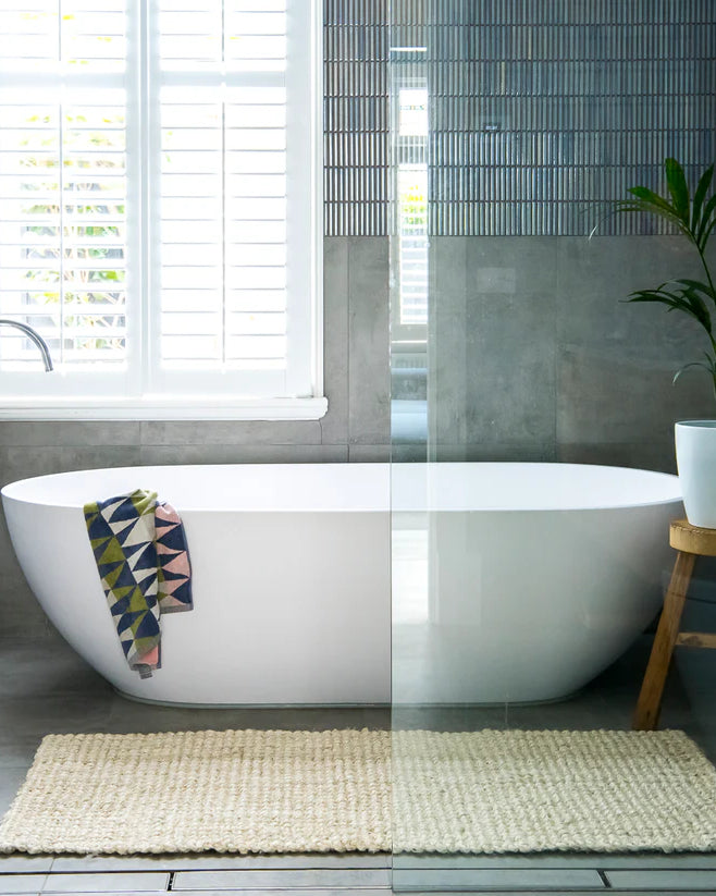 Modern bathroom with a freestanding bathtub, plant, and rug.