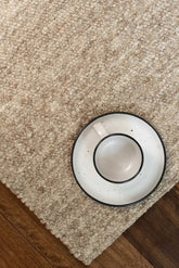 White cup with black rim and saucer on a beige carpet.