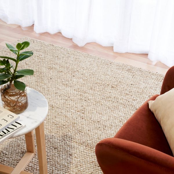 Beige woven rug with a plant and small table in a room setting