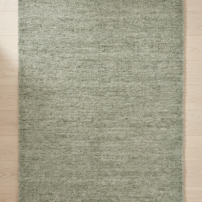 Green rug on a wooden floor with a white vase on the right side.