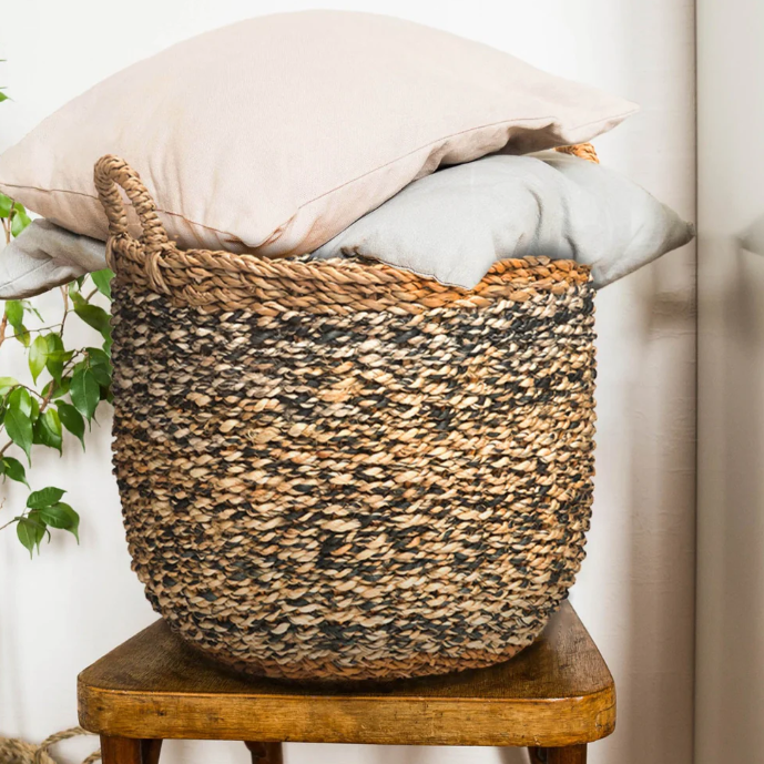 Woven basket with pillows on a wooden stool against a neutral wall.
