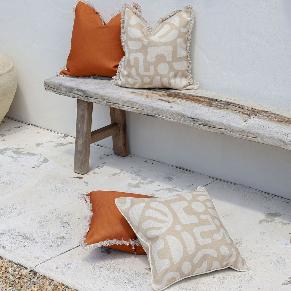 Two patterned pillows on a wooden bench and floor.