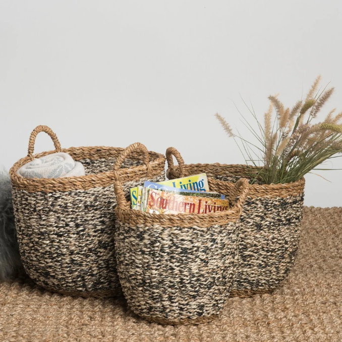 Two woven baskets on a carpeted floor with books and a plant.