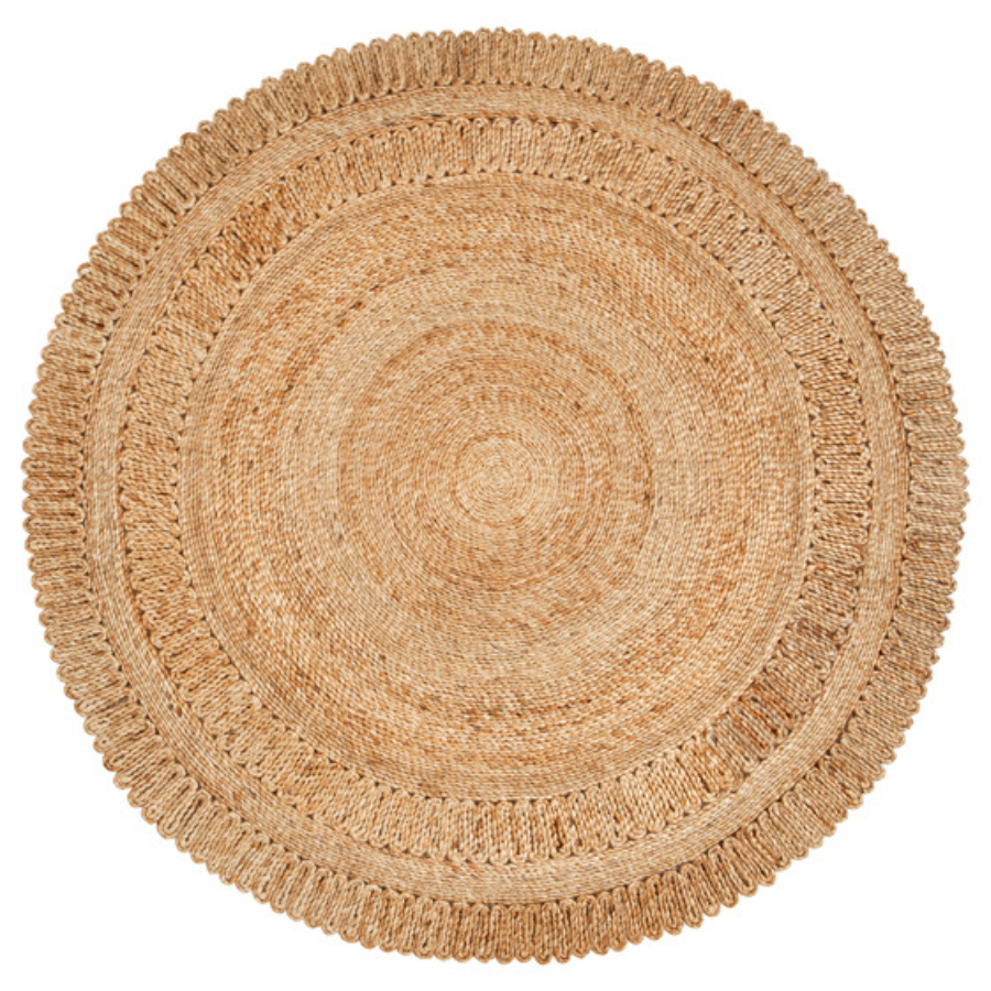 A round natural woven rug made from seagrass or straw, featuring concentric circular patterns and a fringed edge, shown from a top-down view on a white background.