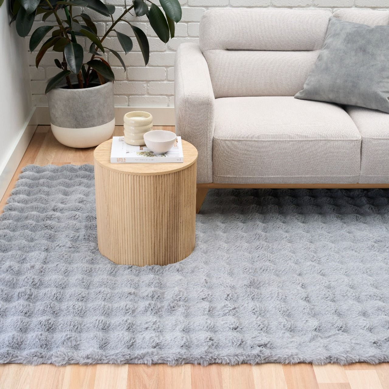 Gray rug on a wooden floor with a beige sofa and side table in the background.