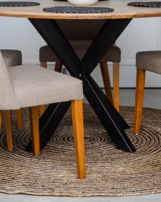 Dining table with black metal legs and wooden chairs on a textured rug.