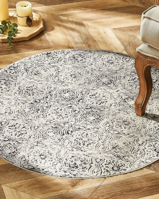 Round patterned rug on a wooden floor with a chair and candle holder in the background.