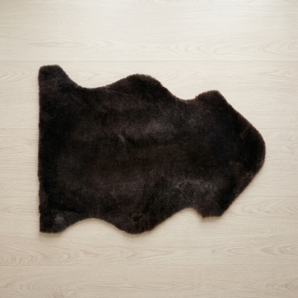 A dark brown shaggy faux fur rug with an irregular hide shape, laid flat on a light beige wood grain floor.