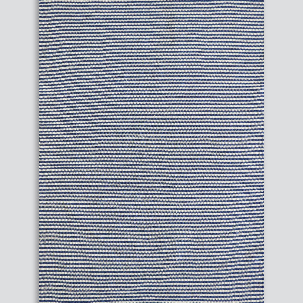 A rectangular woven rug with narrow horizontal navy and off-white stripes, finished with natural beige fringe on the top and bottom edges, shown against a neutral light gray background.