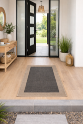 Entryway with a black door, rug, and plants on a light wood floor.