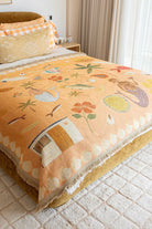 Decorative blanket with floral and nature-themed patterns on a bed in a bedroom.