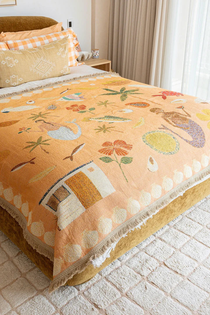 Decorative blanket with floral and nature-themed patterns on a bed in a bedroom.