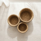 Three round woven natural fiber baskets in different sizes arranged on a light wood floor with soft shadows.