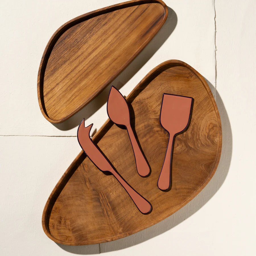 Wooden cutting board with pink cheese knives on a light background