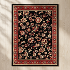 A rectangular area rug with a black field, featuring an intricate floral pattern in red, beige, and cream, surrounded by a detailed red and beige border, shown flat on a light wood plank floor.