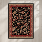 A rectangular black area rug with an intricate traditional floral pattern in red, beige, and cream, displayed flat on a light wood plank floor with soft shadow overlays.
