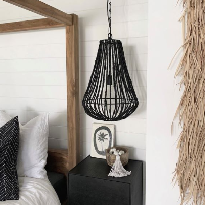 A black woven pendant light hanging in a bedroom setting next to a bed with white bedding and a wooden headboard.