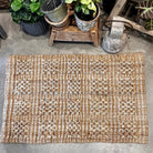 Textured doormat on a concrete floor with potted plants in the background