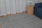 Living room with a gray textured rug, white curtains, a wooden side table, and a blue sofa.