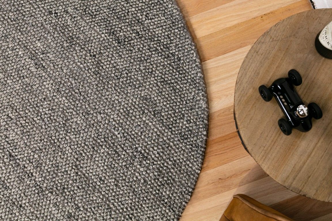 Round gray rug on a wooden floor with a small black toy car on a wooden stool.
