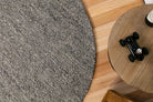 Round gray rug on a wooden floor with a small black toy car on a wooden stool.