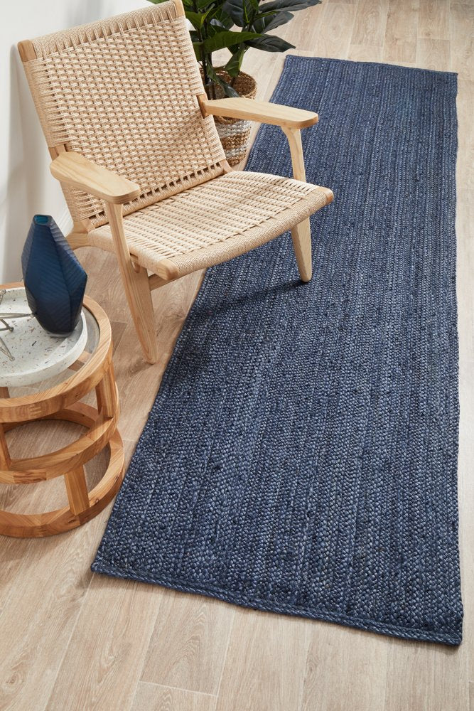Woven blue rug on a wooden floor with a wicker chair and side table.