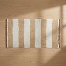A rectangular shag rug with vertical beige and off-white stripes, laid flat on a light oak wood floor with soft shadows.