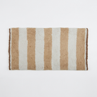 A rectangular shag rug with vertical stripes in warm tan, cream, and light brown, shown flat against a plain white background.