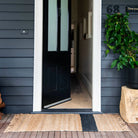 Open door leading into a house with a doormat and plant on a wooden deck.
