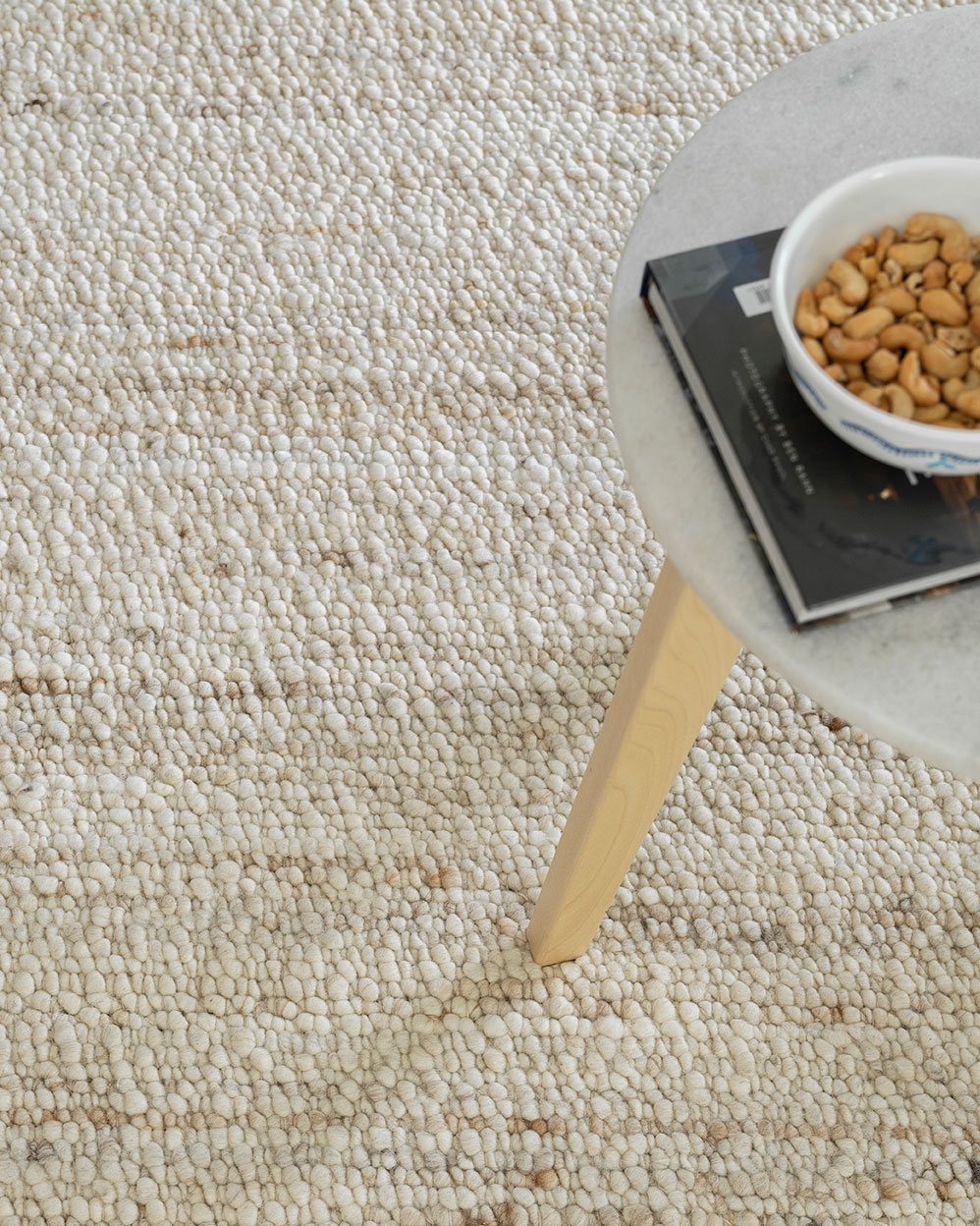 Close-up of a textured beige carpet with a small table and bowl of cat food in the corner.