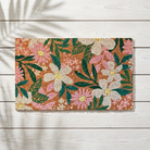 A rectangular coir doormat with a vibrant floral pattern, displayed flat on a white wooden plank floor with soft palm leaf shadows.