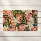 A rectangular coir doormat with a colorful floral pattern, laid flat on a light-colored wooden plank floor.