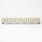 A long, low wicker bench upholstered in an off-white fabric, featuring a scalloped wicker trim along the front and small dark metal feet at the corners, shown against a plain white background.