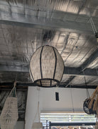 A large woven spherical pendant light hanging from chains in a rustic indoor space with a textured metallic ceiling.