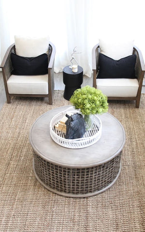 Round wicker coffee table with decorative items in a living room setting.