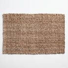 A rectangular woven rug with a textured, braided pattern in shades of brown and beige, shown flat against a light gray background.