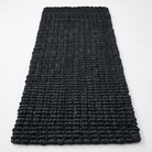 A rectangular black textured rug with a chunky, looped braided pattern, photographed flat against a clean white background.